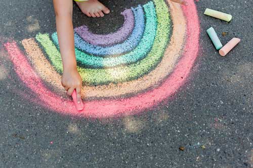 Tavistock Preschool | About us - image of child chalking a rainbow on the ground