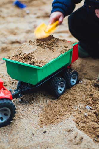 Tavistock Preschool | Home - image of child putting sand into a truck with a trowl
